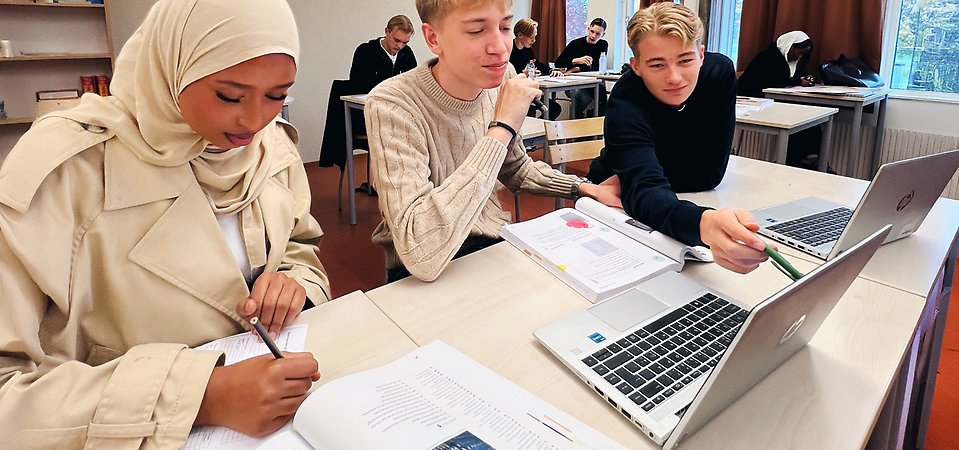 Elever sitter i klassrum. En pekar på en dator och en skriver.