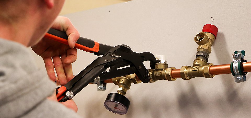 En närbild på någon som skruvar åt kopparrör.
